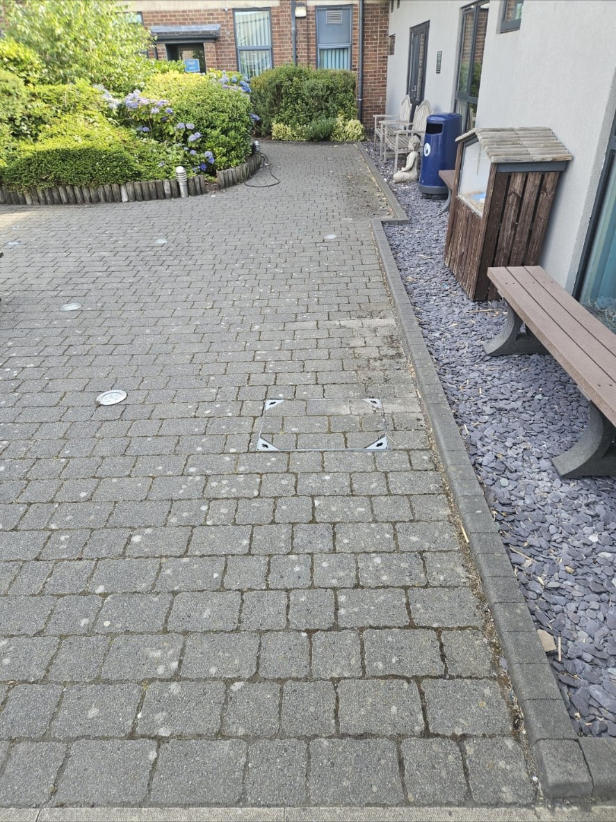 Stained block paved walkway beside a commercial building before cleaning